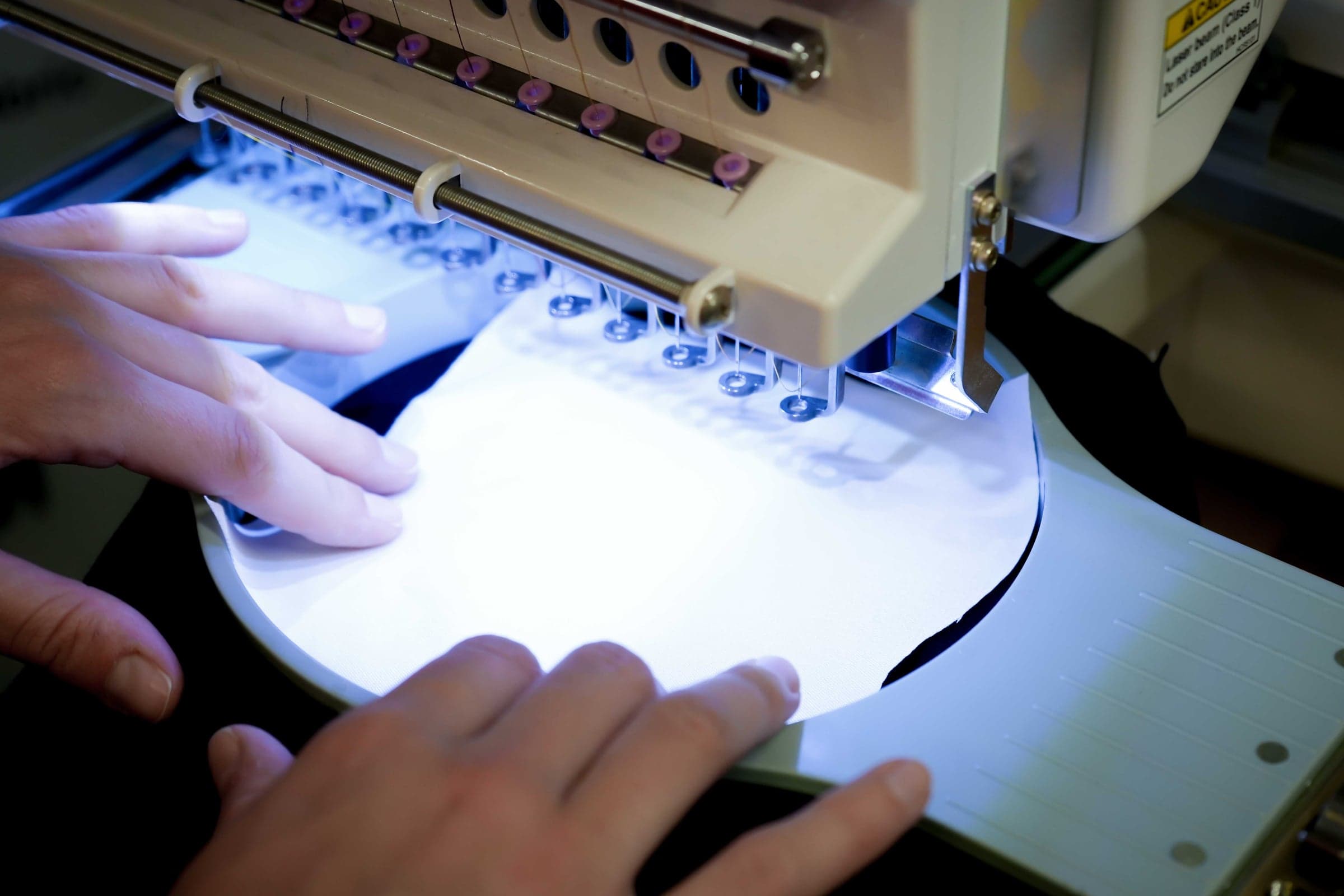Hands placing white top fabric into an embroidery machine for an applique run