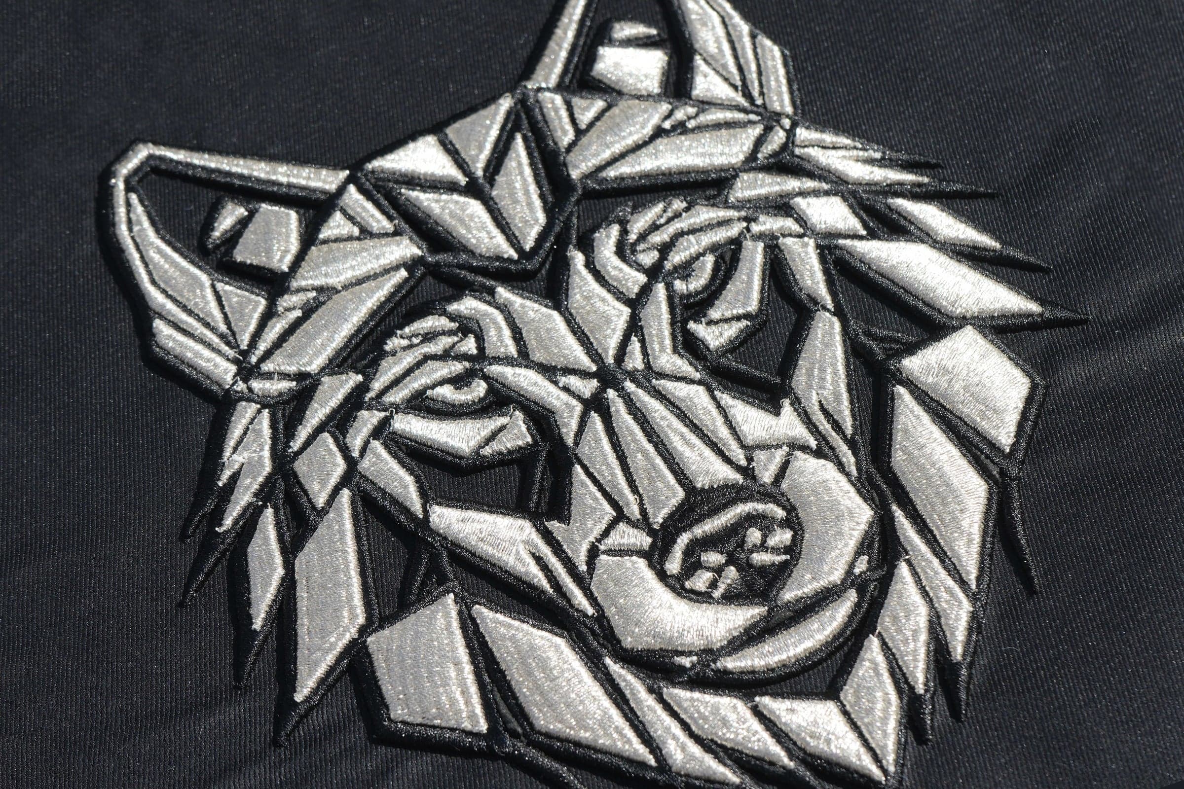Silver geometric wolf head embroidery on dark fabric, single purpose-built placement