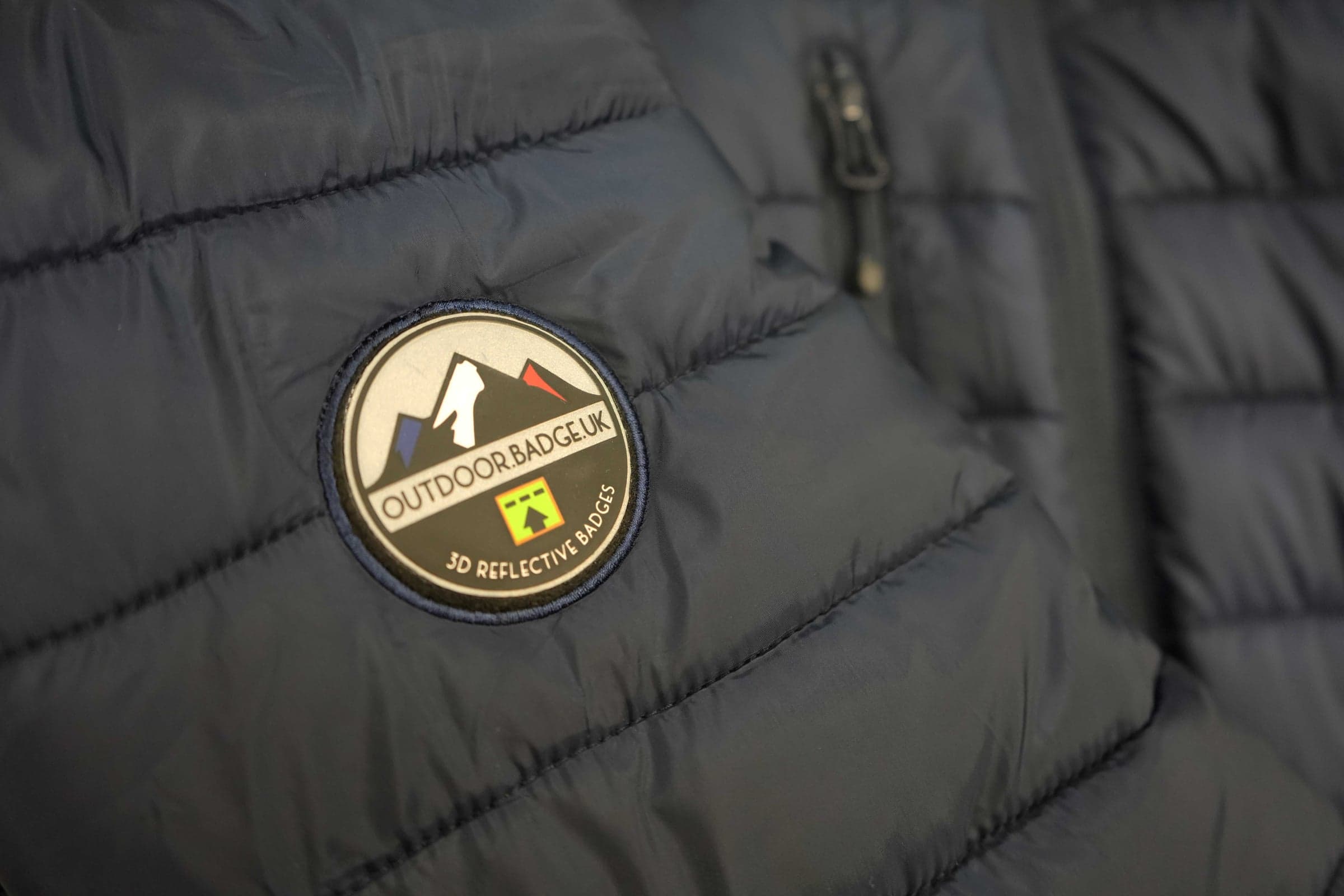 Outdoor.Badge.UK reflective patch stitched onto a navy padded quilted jacket