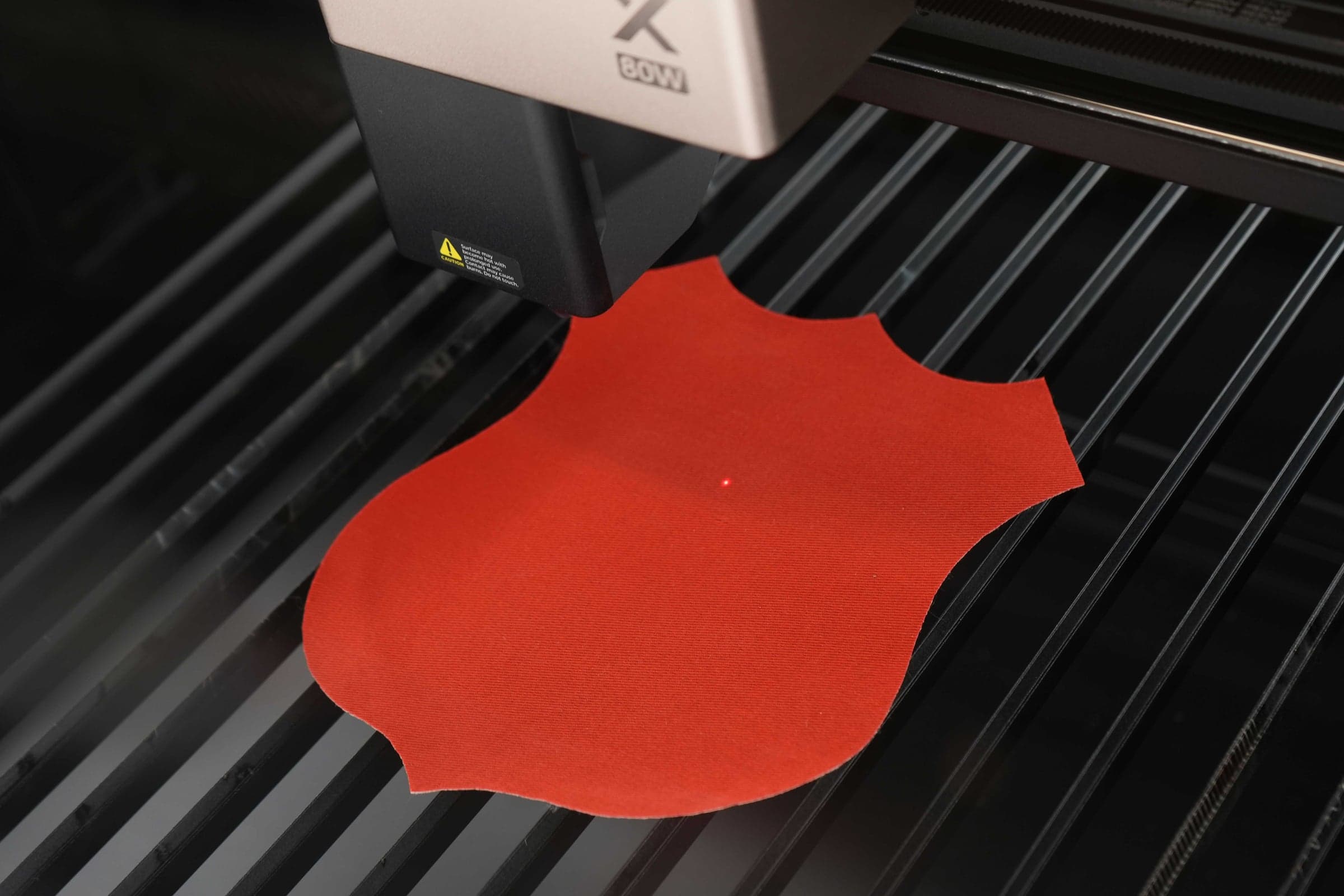 Red shield-shaped felt on an xTool 80W laser cutter bed with targeting dot visible