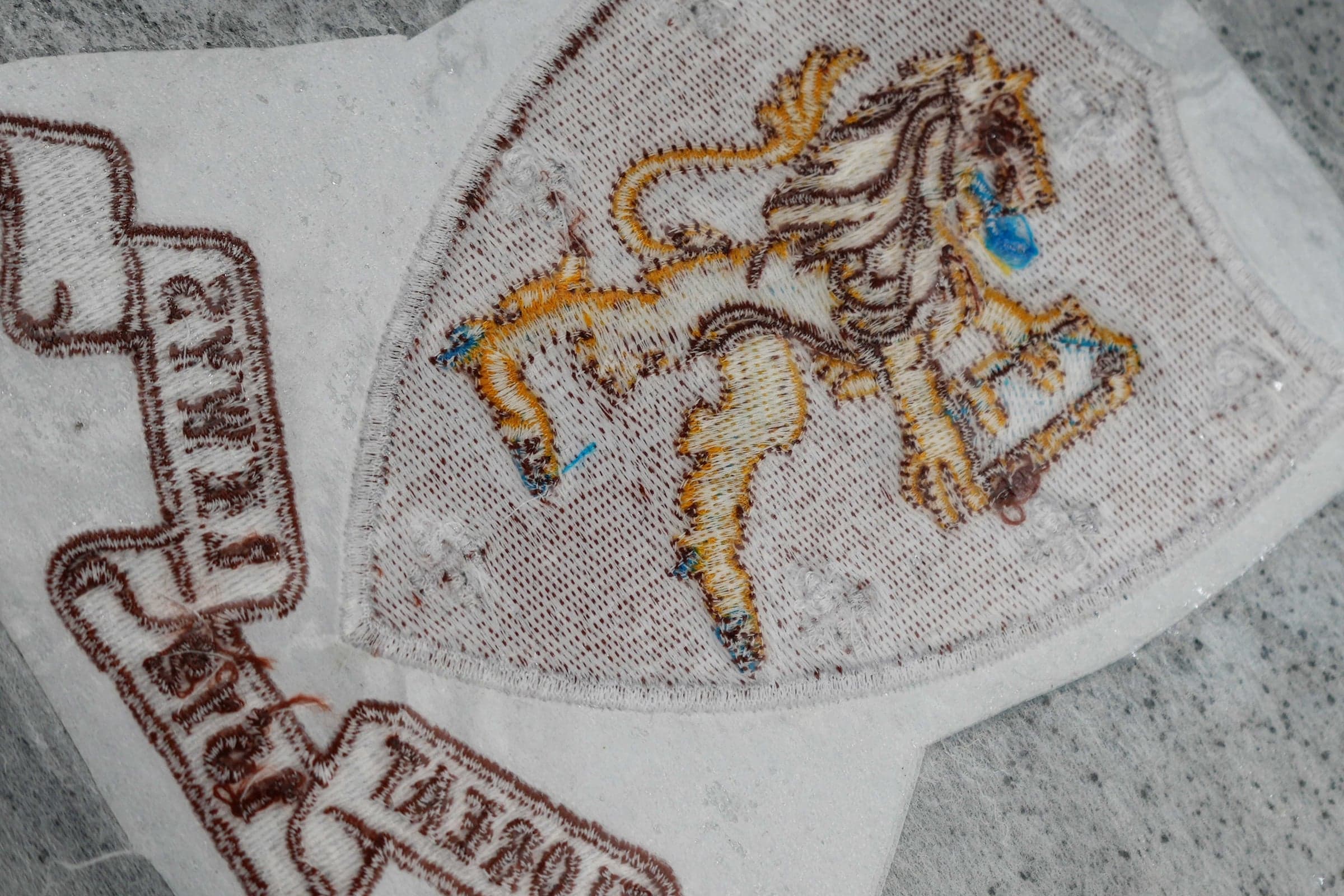 Back/underside of an embroidered patch on white stabiliser showing bobbin and underlay structure