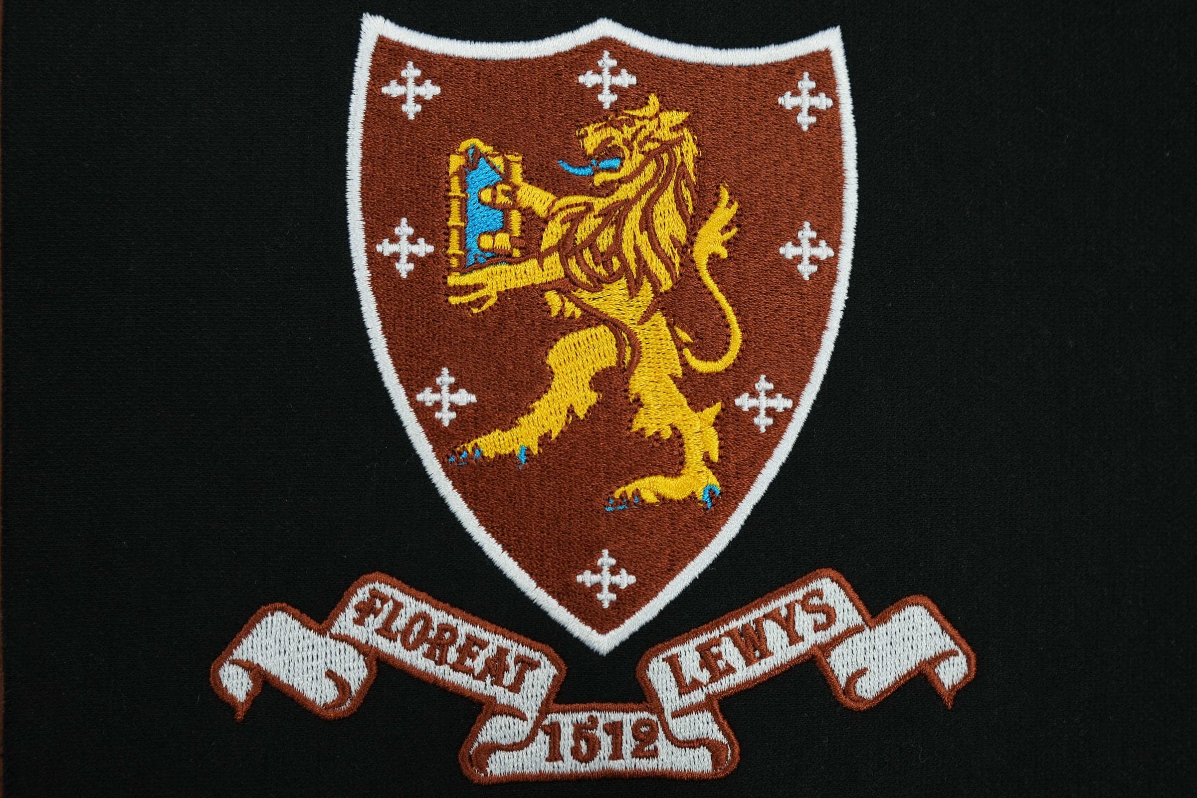 Finished embroidery front — maroon heraldic shield with gold lion rampant and Floreat Lewys 1512 scroll